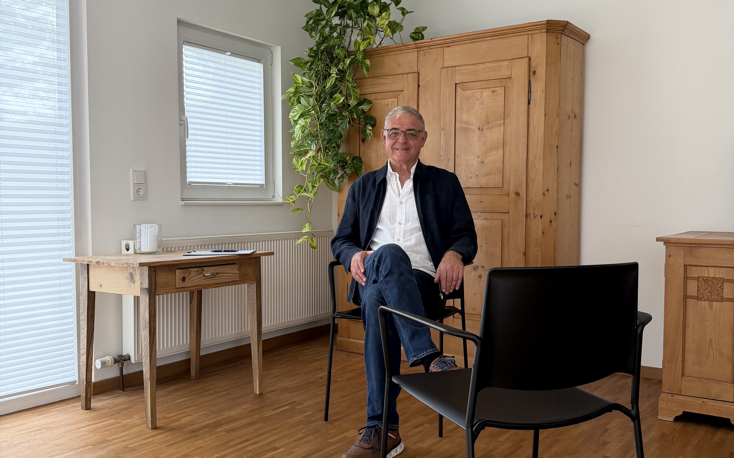 Alois Mennel sitzt ruhig und zugewandt in seinem Praxisraum