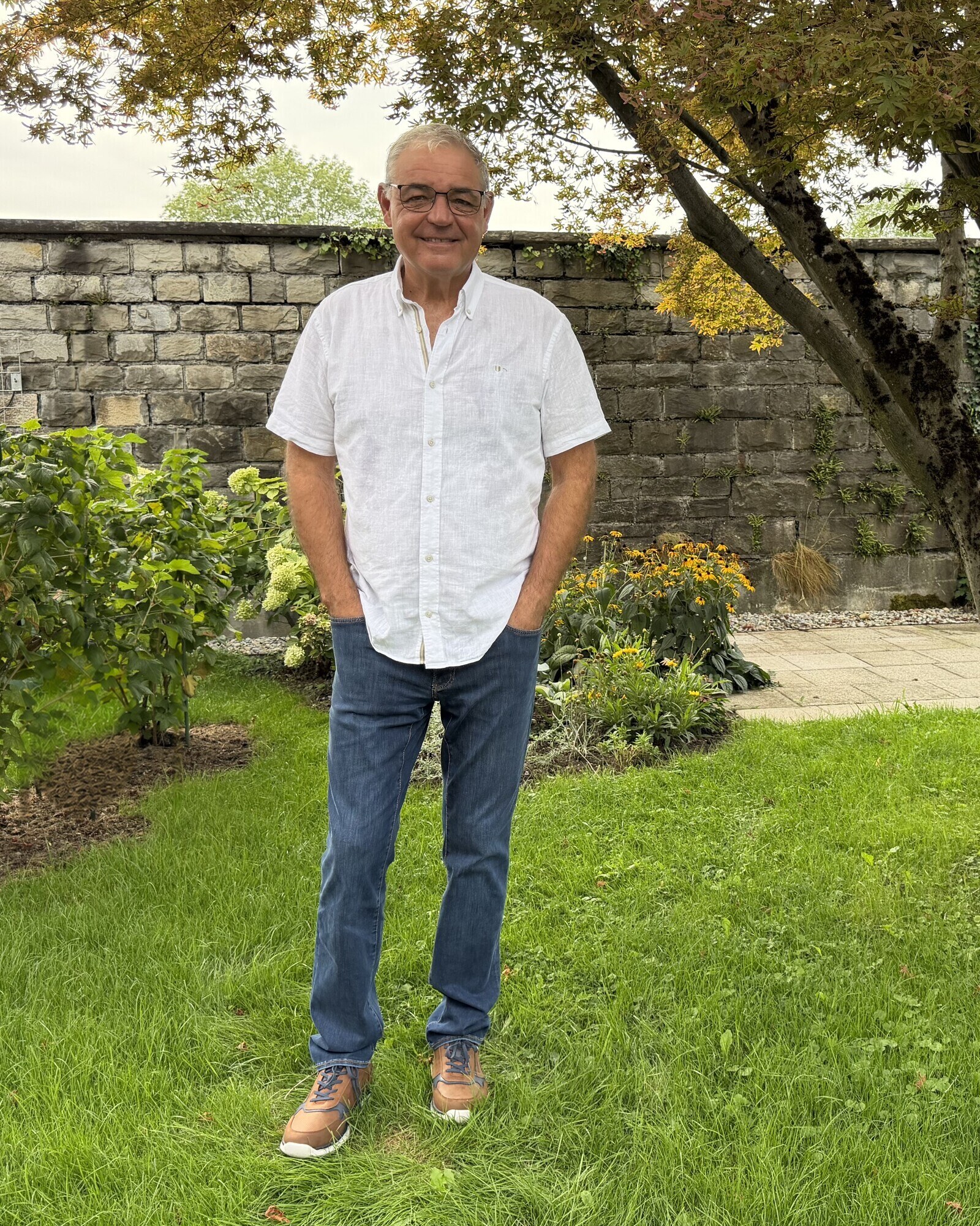 Alois Mennel steht lächelnd in seinem Garten in Hard